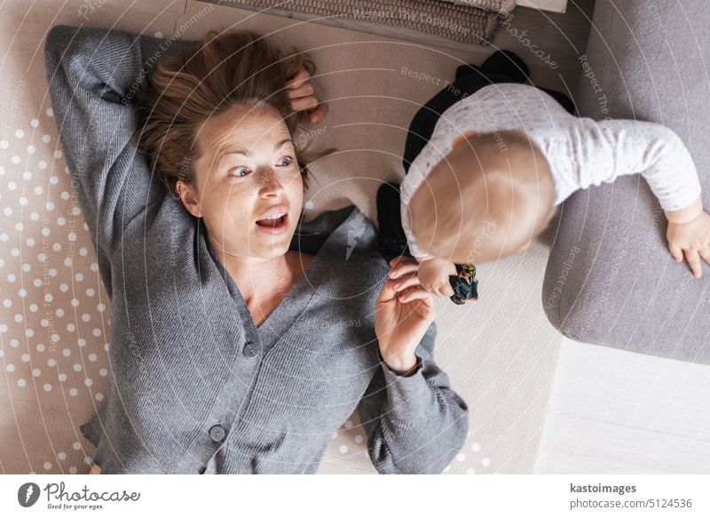 Glückliche Familienmomente. Mutter liegt bequem auf der Kindermatte und spielt mit ihrem kleinen Jungen, der seine ersten Schritte beobachtet und überwacht. Positive menschliche Emotionen, Gefühle, Freude.