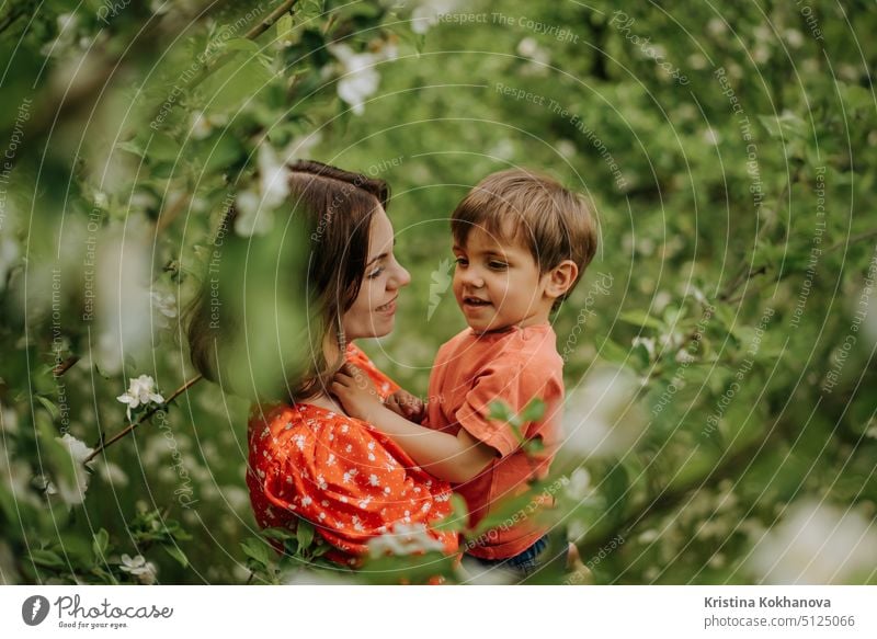 Schöne rührende Szene von Mutter und Kleinkind Sohn in blühenden Frühlingsgarten. Glückliche Mutter und Baby Junge umarmt. Familie, Liebe, Kindheit Konzept.