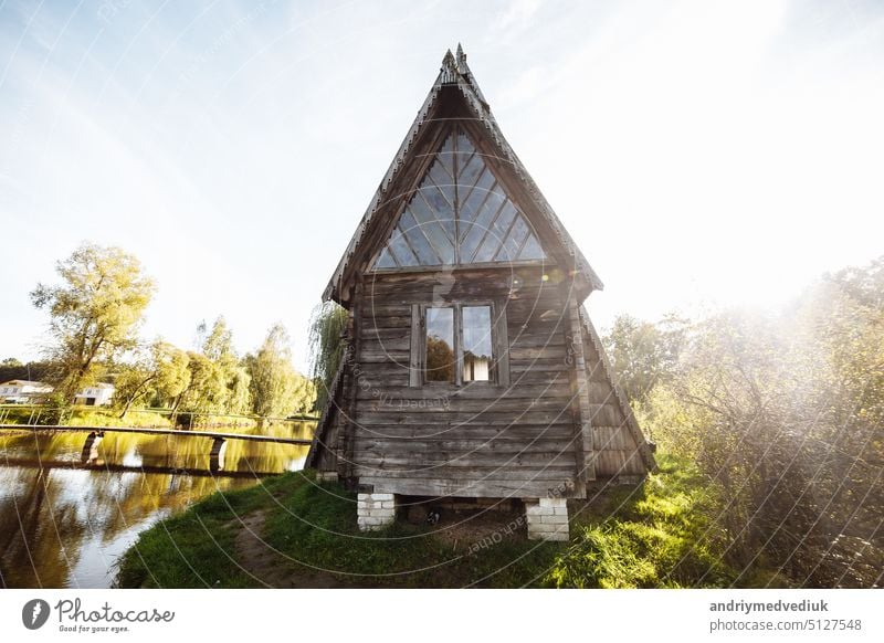 Ein altes hölzernes Dorfhaus steht am Rande des Waldes am See vor dem blauen Himmel. Alte Dorfhütte. Bäuerliche Behausung. Verlassenes Gehäuse Menschen verlassen das Haus.