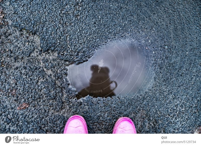 Spieglein Spieglein ..in der Pfütze Spiegelung Gummistiefel rosa Asphalt Mütze grau Struktur Wolken Wasser Regen Straßen Bommelmütze Winter Tageslicht von oben