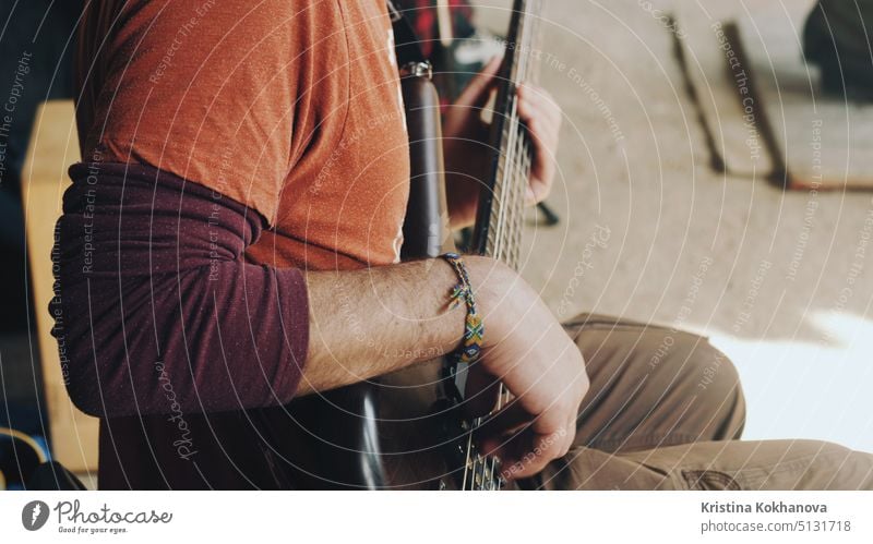 Mann spielt die Bassgitarre beim Konzert auf der Straße. Nahaufnahme von Gitarrist spielt auf braunem Holz Musikinstrument. Straßenmusiker mit einem geflochtenen Hippie-Armband am Arm.