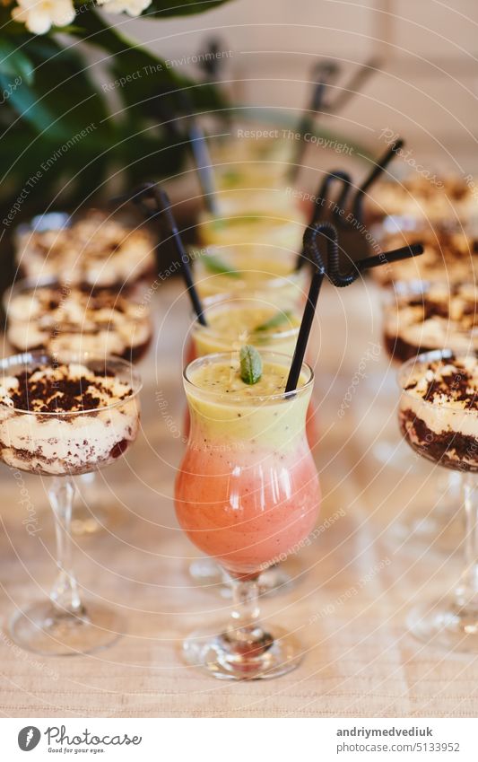 Sommerliche kalte Cocktails mit einem Becher Limonadenwasser. Verschiedene Limonaden mit Eiswürfeln und Zitronenscheiben in Einmachgläsern stehen auf einem Holztisch