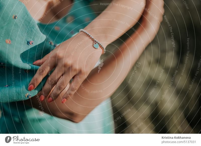 Weibliche Hand mit Silberperlen Armband und blauem Herz Charme. Türkisfarbenes Schmuckzubehör. Kleid im Retro-Stil. schön Schönheit Eleganz teuer Mode Frau