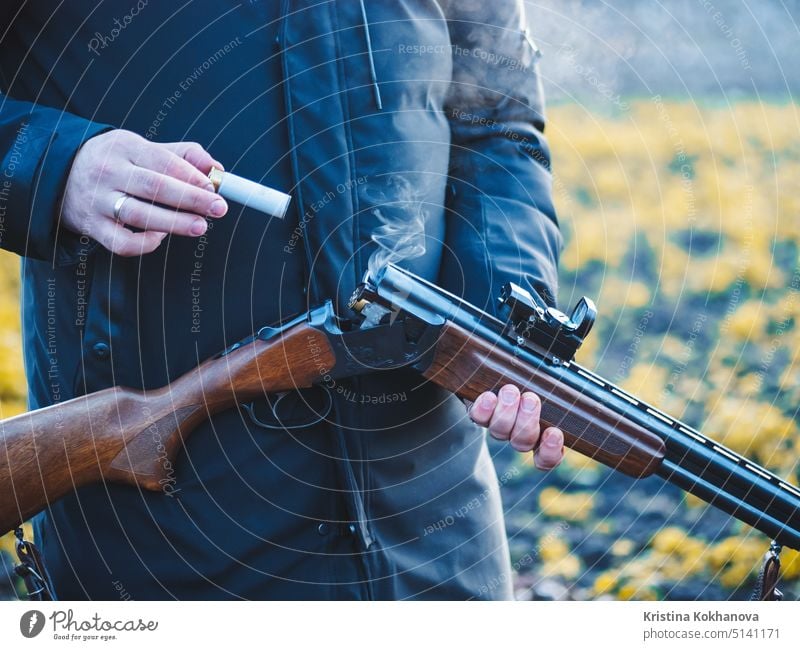 Sportschießen. Jäger beim Nachladen einer Patrone im Feld. Rauch aus dem Schaft eines Jagdgewehrs mit glattem Lauf nach dem Abschuss. 12 Aktivität zielen