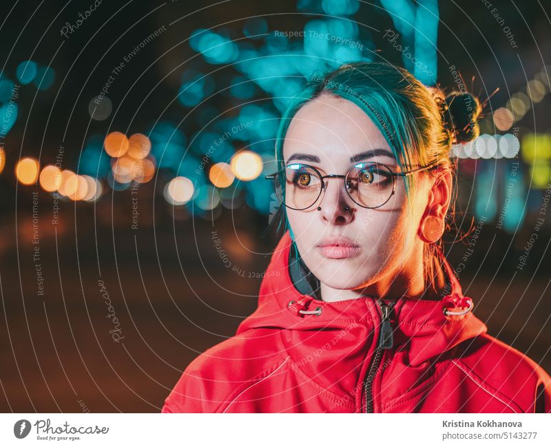 Junge schöne Mädchen mit blau gefärbten ungewöhnliche Haare, transparente Brille, Piercing stehen in der Nacht Straße mit Neonröhren Hintergrund. Porträt des glücklichen niedlichen stilvollen Teenager.