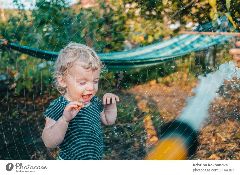 Lustige Reaktion von Baby-Junge während Wasser Kampf Spiel mit Schlauch. Kleinkind spielen, abkühlen bei heißem Wetter - Sommer oder Frühling Saison. Person