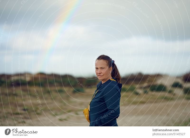 Nachdenklich in die Kamera blickende Frau mittleren Alters mit einem Regenbogen im Hintergrund, Konzept für Zukunftsaussichten nachdenklich Ausdruck Stehen