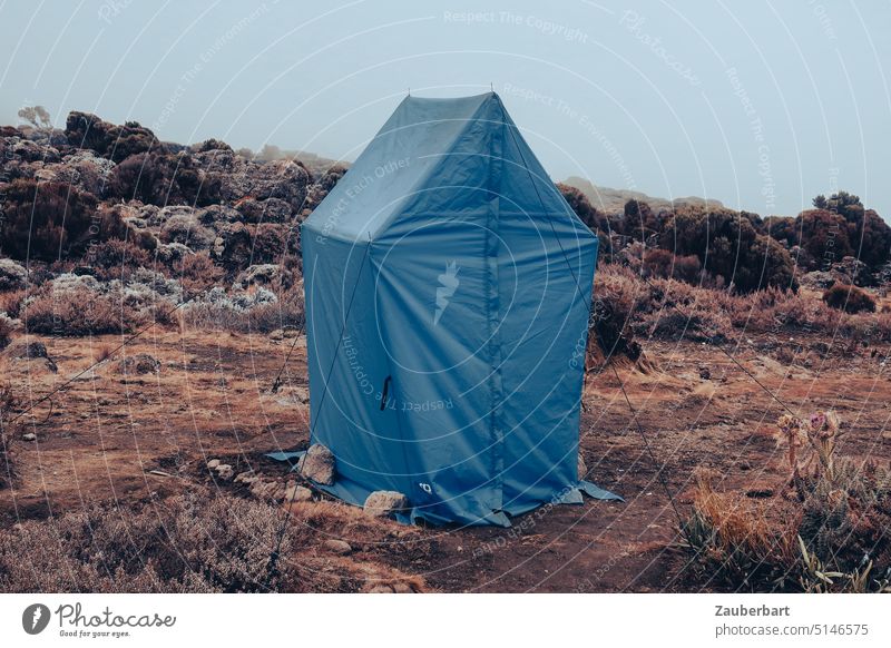 Kleines blaues Toiletten-Zelt vor felsiger Landschaft am Kilimanjaro, Shira Camp 2 Felsen Felsbrocken Nebel Wolken Wandern Trekking Bergsteigen Abenteuer