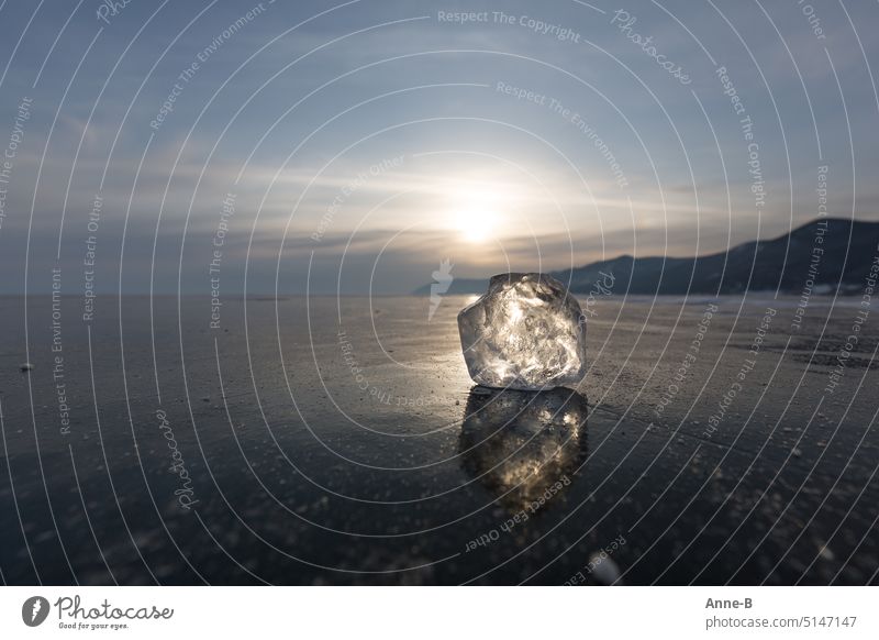 schöner großer glitzernder Eisklumpen auf einem dick zugefrorenen See in Sibirien ( Baikal ) , im Hintergrund die langsam untergehende Sonne und ein paar Hügel.