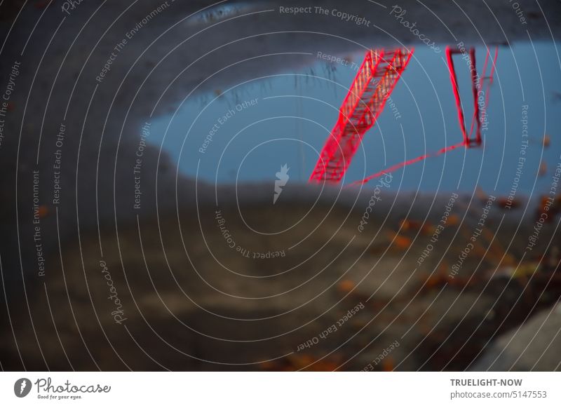 An einer Baustelle in einer Wasserpfütze auf Sandboden spiegelt sich ein großer roter Bau-Kran vor blauem Himmel Pfütze Spiegelung Erde wolkenlos Technik