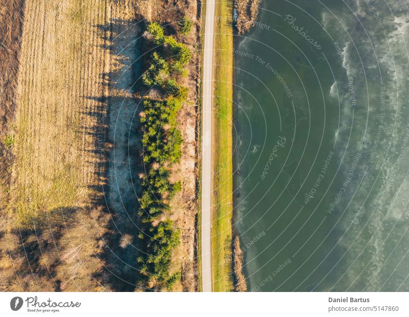 Sonnenuntergang über einem zugefrorenen See. Sonnenstrahlen fallen auf das Wasser. Schatten von Bäumen auf dem Eis, das den See bedeckt. Luftaufnahme eines zugefrorenen Sees. Eisdecke im Hintergrund. Gefrorenes Gras im Wasser