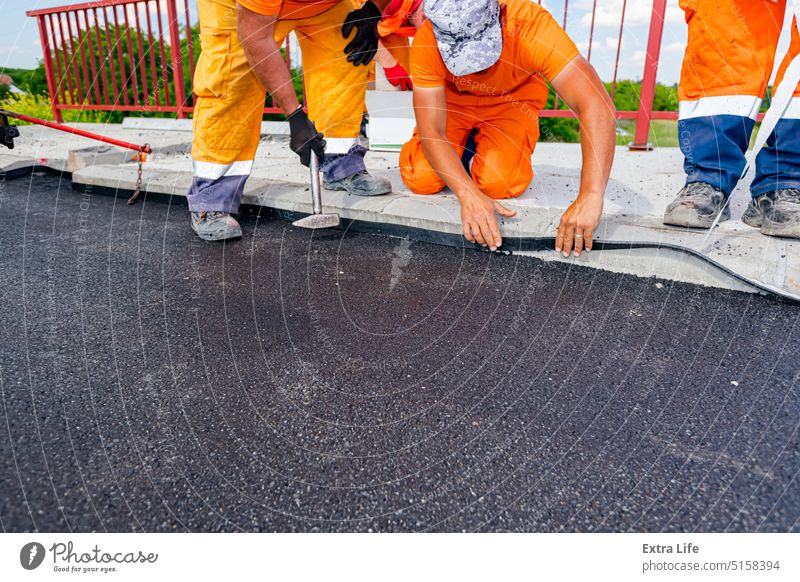 Arbeiter bringen schwarze Bitumenbahnen zur Abdichtung von Straßen und Brücken am Rand des Bürgersteigs an bewerben Asphalt befestigen bituminös erbaut Kollege