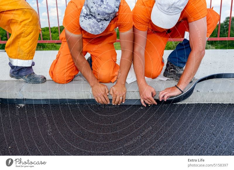 Arbeiter bringen schwarze Bitumenbahnen zur Abdichtung von Straßen und Brücken am Rand des Bürgersteigs an bewerben Asphalt befestigen bituminös erbaut kreisen