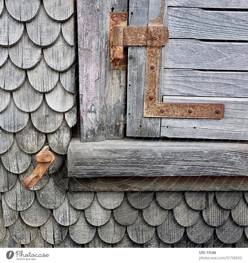 Alte, schuppige Hauswand mit verrammelter Fensterklappe. Holzhaus Vergangenheit Holzfliesen Außenaufnahme Menschenleer Hütte alt Holzhütte Scharnier Fassade