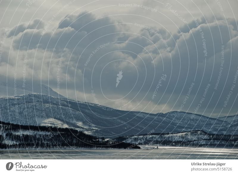 Hafeneinfahrt mit kleinem Leuchtturm, Siedlung und Wolkenbergen an der winterlichen norwegischen Küste Winter winterliche Küste kaltes Meer Wellen auf dem Meer