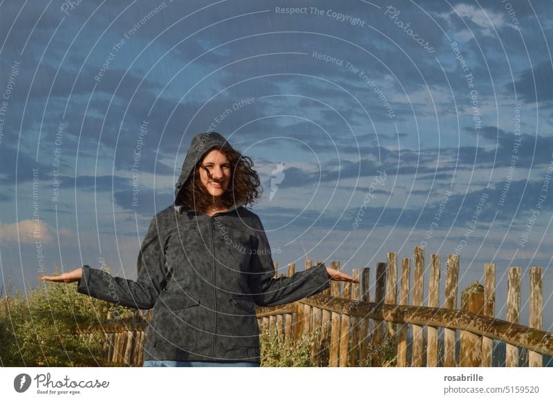 na und? - junge Frau steht im Regen und lächelt Wetter Unwetter trotzdem lächeln unbeeindruckt optimistisch gute Laune Frohnatur fröhlich egal problemlos