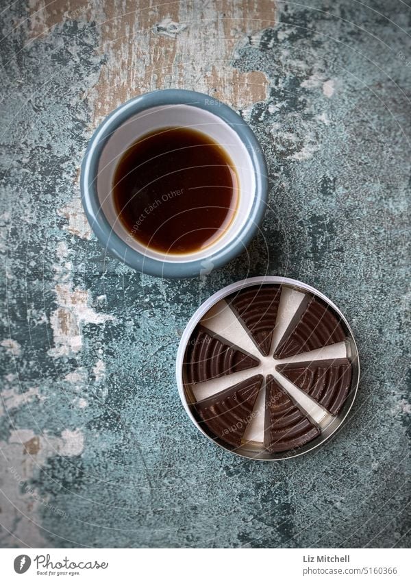 Draufsicht auf eine Tasse schwarzen Kaffee und eine Dose Schokoladendreiecke auf einer beschädigten Tafel Kaffeepause Kaffeetrinken Getränk Kaffeetasse genießen