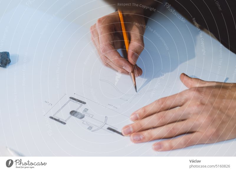 Nahaufnahme eines aufgeweckten, geschäftstüchtigen, aufstrebenden und jungen Architekten an seinem Schreibtisch in seinem Büro. Er zeichnet ein neues Produkt auf weißem Papier. Die Arbeit eines Produktdesigners