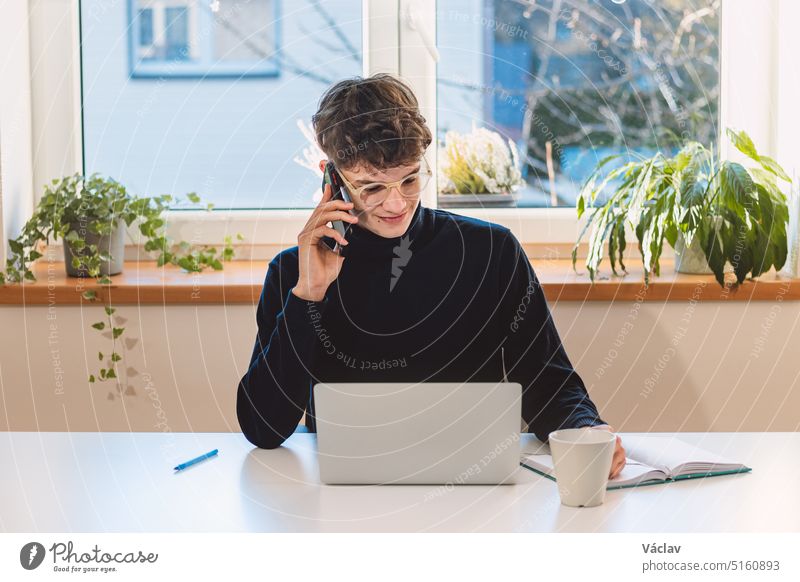 Ein zielstrebiger Geschäftsmann mit braunen Haaren telefoniert mit einem aufregenden Kunden und macht sich Notizen in seinem Terminkalender. Online-Geschäftsbesprechung mit einem Kunden. Junger Visionär