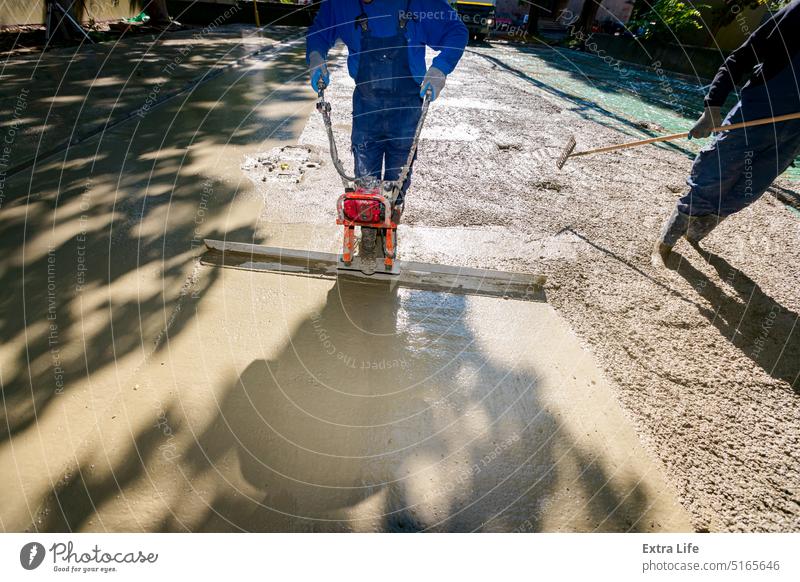 Ein Arbeiter benutzt ein Motorgerät, einen Verdichter, um frischen Beton einzuebnen und zu verdichten. Ausrichten Baustelle gießen Zement Tiefbau kompakt