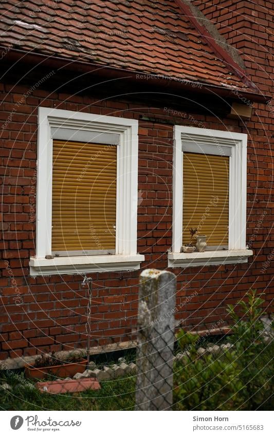 Backsteinfassade mit geschlossenen Rollläden Rollladen Fenster doppelt Paar paarweise Jalousie Fassade Vorgarten Siedlung Dorf Zaun Eigentum privat Privatsphäre