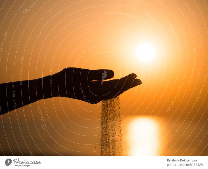 Silhouette eines jungen Mädchens, das mit der Hand Sand von einem Strand schüttet, vor einem gelben Himmel bei Sonnenuntergang Natur Meer Erwachsener