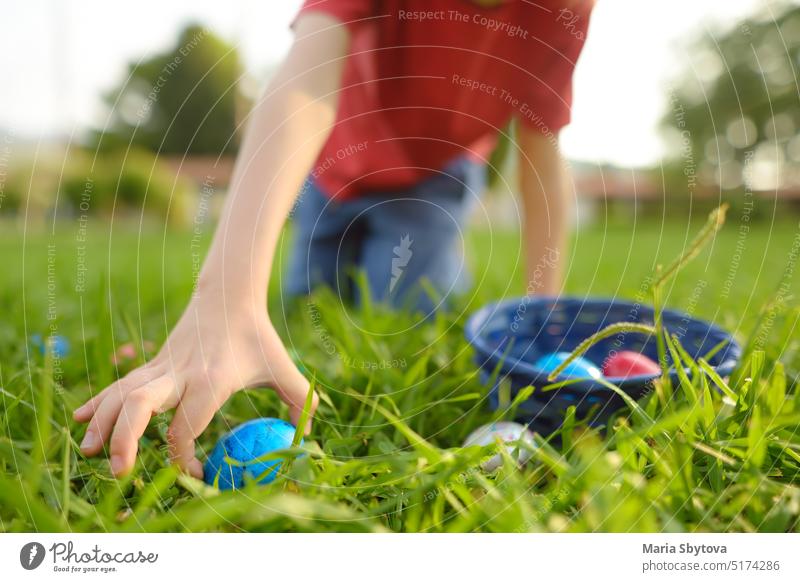 Kleiner Junge auf Eiersuche im Frühlingsgarten am Ostertag. Traditionelles Fest im Freien. Kind feiert Osterfest. Fokus auf Hand. Ostern Suche Garten jagen