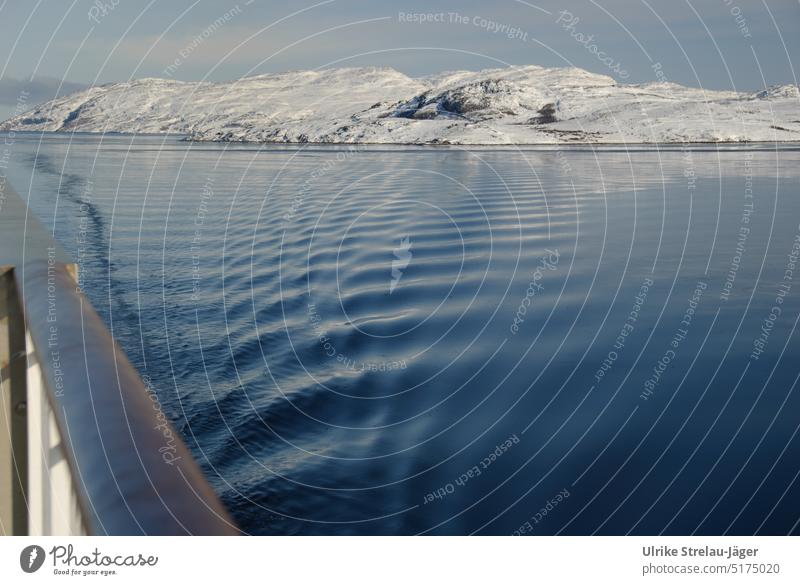 Schiffsreling mit Wellen auf eisigem Meer und Küste mit schneebedeckten Hügeln Reling Meer im Winter Winterstimmung Wellen auf dem Meer