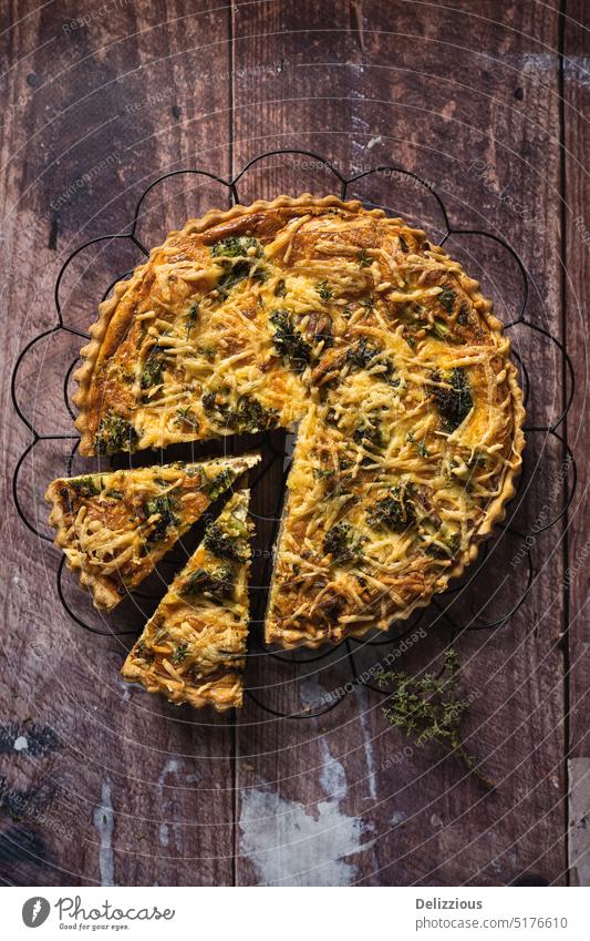 Draufsicht auf eine leckere Brokkoli-Quiche auf einem Holztisch, mit ausgeschnittenem Stück Torte Pasteten Französisch Bohnenkraut Lebensmittel backen gebacken