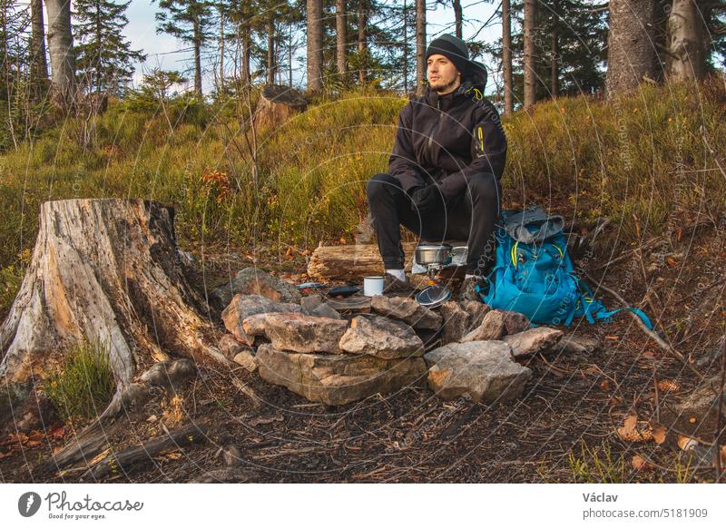 Trekking-Enthusiasten in der Wildnis sitzen am Lagerfeuer und genießen das Frühstück bei Sonnenaufgang. Frühstücken und Vitamin D tanken auf dem Gipfel eines Hügels. Das Leben eines naturverbundenen Jungen