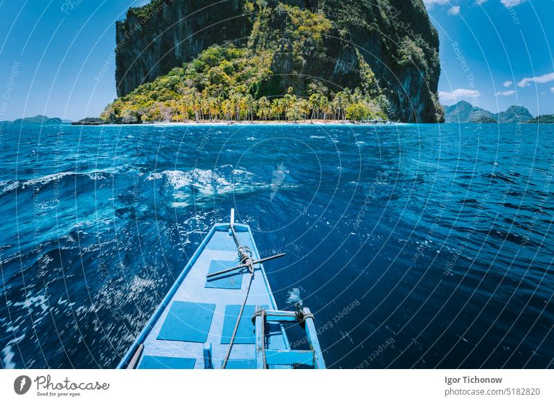 Ein traditionelles Banca-Boot nähert sich einem kleinen Ipil-Strand vor der kreisrunden Insel Pinagbuyatan mit riesigen Kalksteinfelsen, die mit Kokospalmen bewachsen sind. El Nido, Palawan, Philippinen