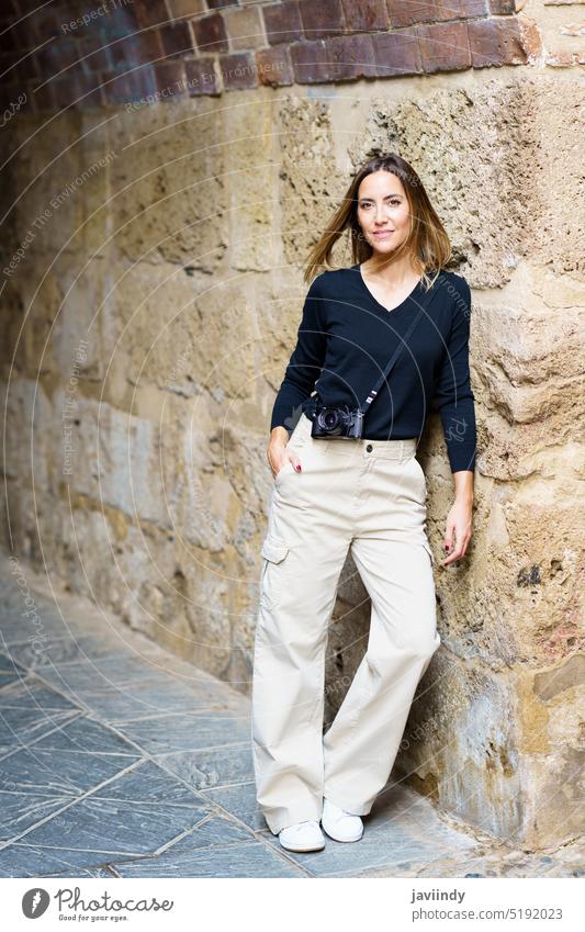 Glückliche Frau mit Fotokamera an einer verwitterten Mauer in der Altstadt lehnend Tourismus Lächeln positiv Urlaub Straße Sightseeing Fotoapparat reisen