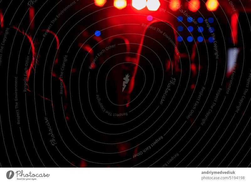 jubelnde Menge vor hellen roten Bühnenlichtern. Silhouette Bild der Menschen tanzen in Disco-Nachtclub oder Konzert bei einem Musikfestival. Beifall spendend