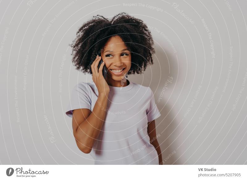 Studio-Porträt einer fröhlichen dunkelhäutigen Frau, die sich mit einem Mobiltelefon unterhält Sitzen jauchzen Blick Amerikaner Lächeln heimwärts niedlich