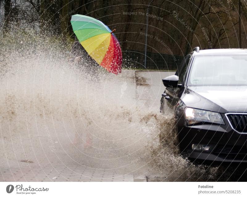 Wusch die Zweite!!! Das dunkle Auto fährt rücksichtslos mit hoher Geschwindigkeit durch eine tiefe Pfütze. Ein riesiger Wasserschwall durchnässt die Fußgängerin mit einem bunten Regenschirm. Die roten Gummistiefel sind nicht mehr zu sehen.