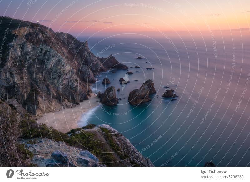 Sonnenuntergang über dem versteckten surrealen Strand Praia Da Ursa. Cabo Da Roca mit Leuchtturm im Hintergrund. Atlantikküste, Portugal, Europa Abenddämmerung