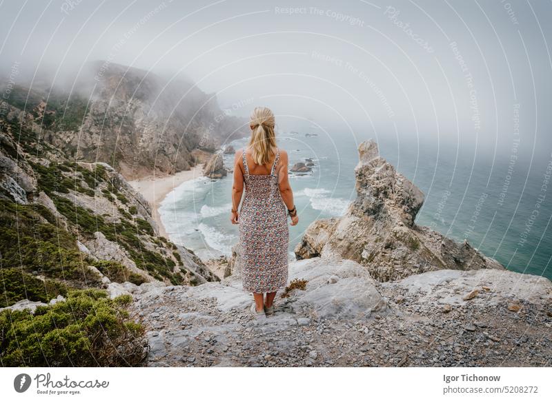 Erwachsene weibliche Aufenthalt und genießen Praia da Ursa Strand am Morgen. Surreale neblige Landschaft von Sintra, Portugal. Atlantischer Ozean Küstenlinie Landschaft