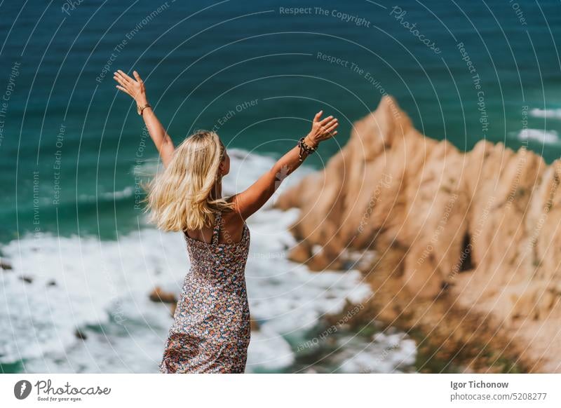 Schöne blonde Frau, die die Hände hebt und den Strand Praia da Ursa genießt. Surreale Szenerie von Sintra, Portugal. Atlantischer Ozean Küstenlinie Landschaft