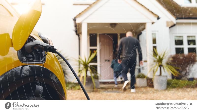 Aufladen eines Elektroautos in der Einfahrt vor dem Haus mit der Familie im Hintergrund elektrisch PKW heimwärts außerhalb Fahrweg Gebühr Stecker Anschluss