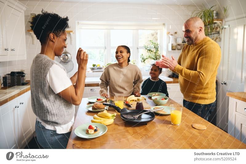 Junge mit Down-Syndrom isst Pfannkuchen zum Frühstück mit seinen Eltern Familie Gesundheit Genuss rassenübergreifend Küche Lebensmittel Klatschen Arbeitsplatte