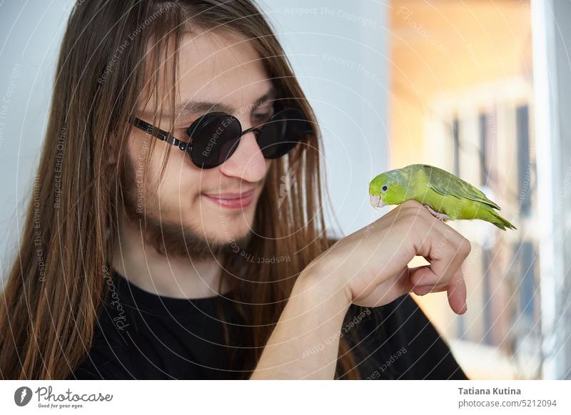 Ein Mann mit langen Haaren kommuniziert mit einem Papageienforpus Haustiere Papageienvogel exotisch Schnabel Pflege gelb Feder Lifestyle tropisch Porträt