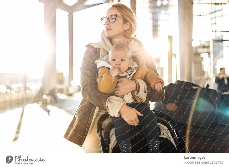 Motherat Reisen mit seinem Säugling Junge Kind, zu Fuß, Schieben Kinderwagen und Gepäckwagen vor dem Flughafen-Terminal Station. reisen Baby Urlaub Ausflug