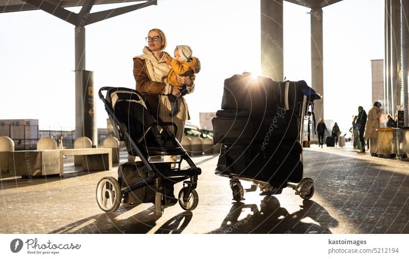 Motherat Reisen mit seinem Säugling Junge Kind, zu Fuß, Schieben Kinderwagen und Gepäckwagen vor dem Flughafen-Terminal Station. reisen Baby Urlaub Ausflug