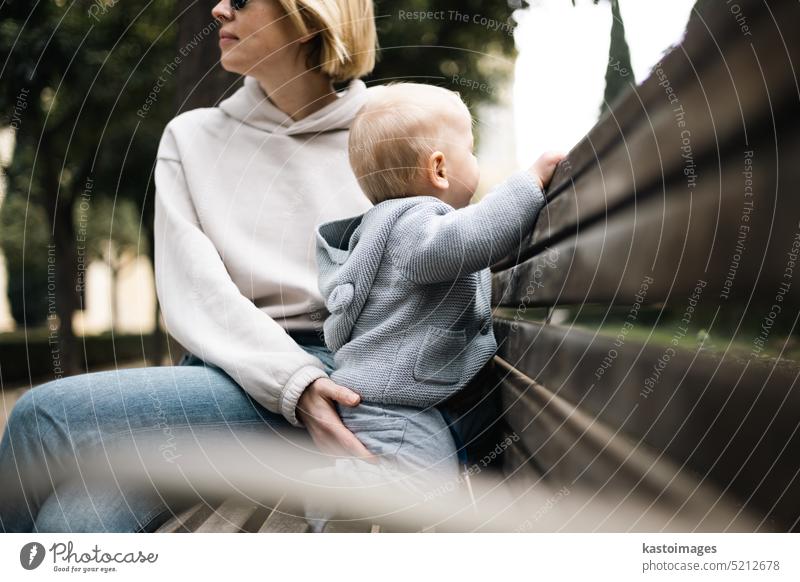 Junge Mutter mit ihrem süßen Säugling auf einer Bank im Stadtpark sitzend Sohn jung Lifestyle Kind Liebe wenig Familie Park Baby Frau Sitzen Zusammensein heiter