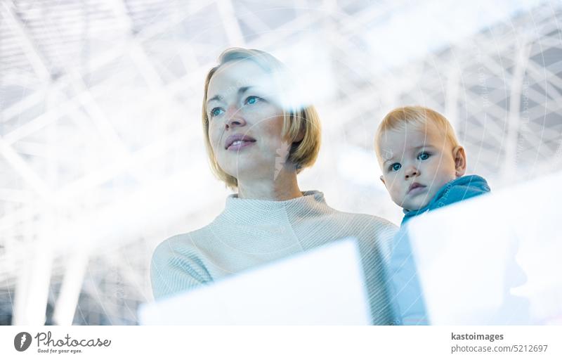 Nachdenklich junge Mutter Blick trough Fenster hält sein Baby Junge Kind beim Warten auf ein Flugzeug am Flughafen Terminal Abflugtore Bord. Reisen mit Baby-Konzept.