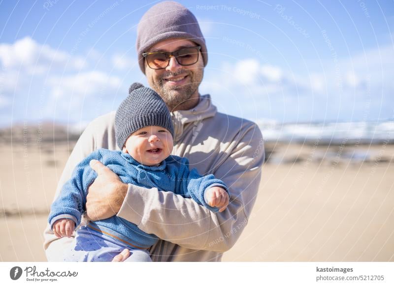 Vater genießt die reine Natur und spielt mit seinem kleinen Sohn am windigen Sandstrand von Famara, Insel Lanzarote, Spanien. Familie Reisen und Elternschaft Konzept.