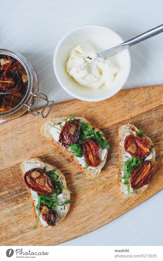 traditionelle italienische Bruschetta - Brottoast mit sonnengetrockneten Tomaten, Frischkäse, Olivenöl und Rucola. Belegtes Brot Lebensmittel Zuprosten Snack