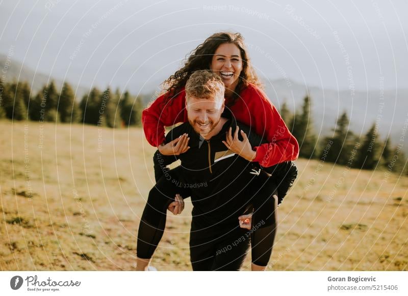 Junge Frau reitet huckepack auf einem Freund in Green Hills aktiv Aktivität Erwachsene Abenteuer Rucksack Kaukasier Landschaft Paar lockig Feld Freiheit Freunde