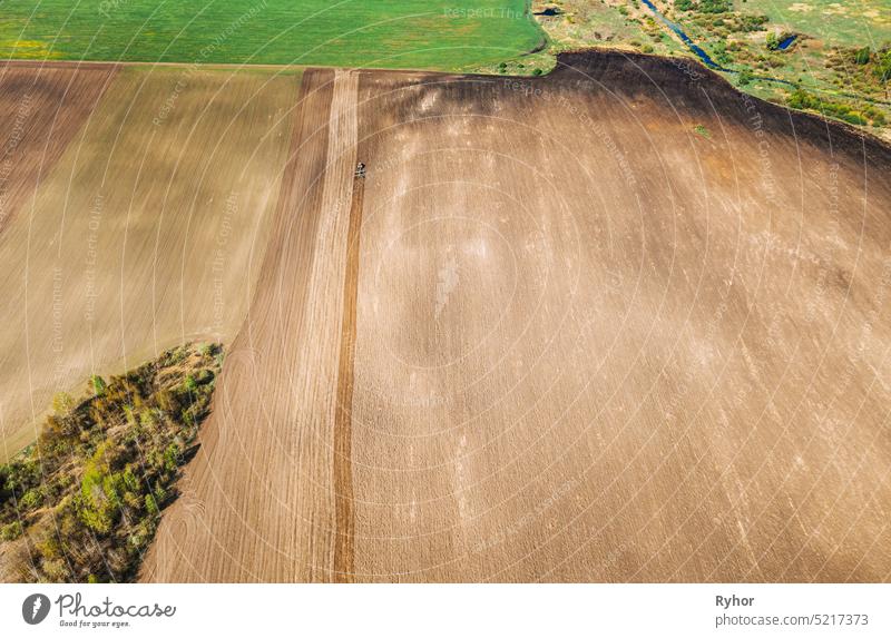 Traktor pflügt Feld im Frühling. Beginn der landwirtschaftlichen Saison. Grubber gezogen von einem Traktor in der Landschaft ländlichen Feld. Ländliches Feld Landschaft. Luftaufnahme. Top Flachansicht