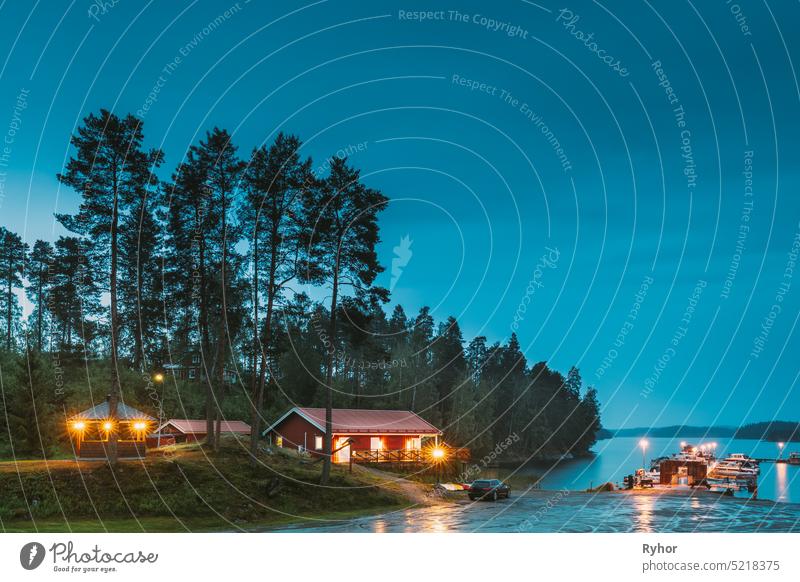 Schweden. Schweden. Schöne rote schwedische Holzblockhaus Haus auf felsigen Insel Küste im Sommer Nacht Abend. See oder Fluss Landschaft. Schöne hölzerne Pier in der Nähe von See im Sommer Abend Nacht. See oder Fluss Landschaft. Flussufer.